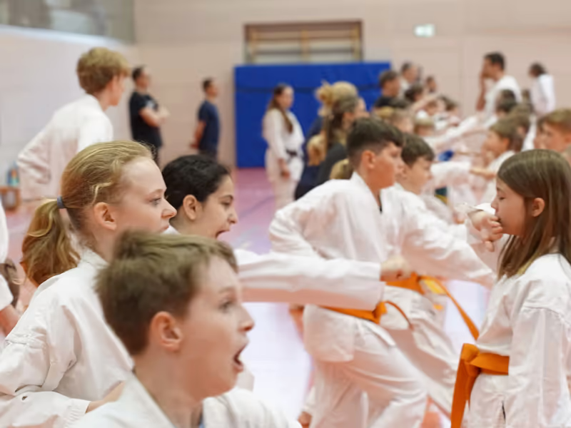 Eine lange Reihe Kinder im Karateanzug &uuml;bt mit lautem Kiai den Fauststo&szlig;, vorne ein Junge mit offenem Mund