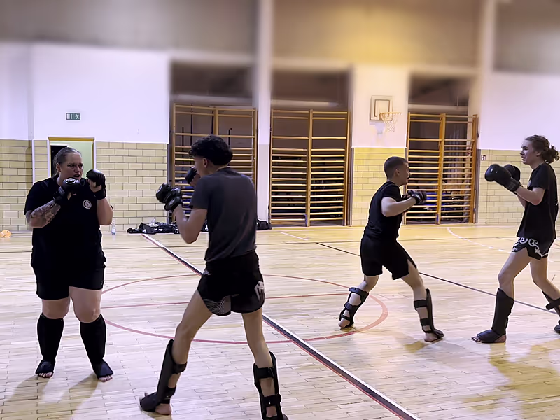 Zwei Paare beim Sparring in der Sporthalle, alle mit Boxhandschuhen und Schienbeinschonern