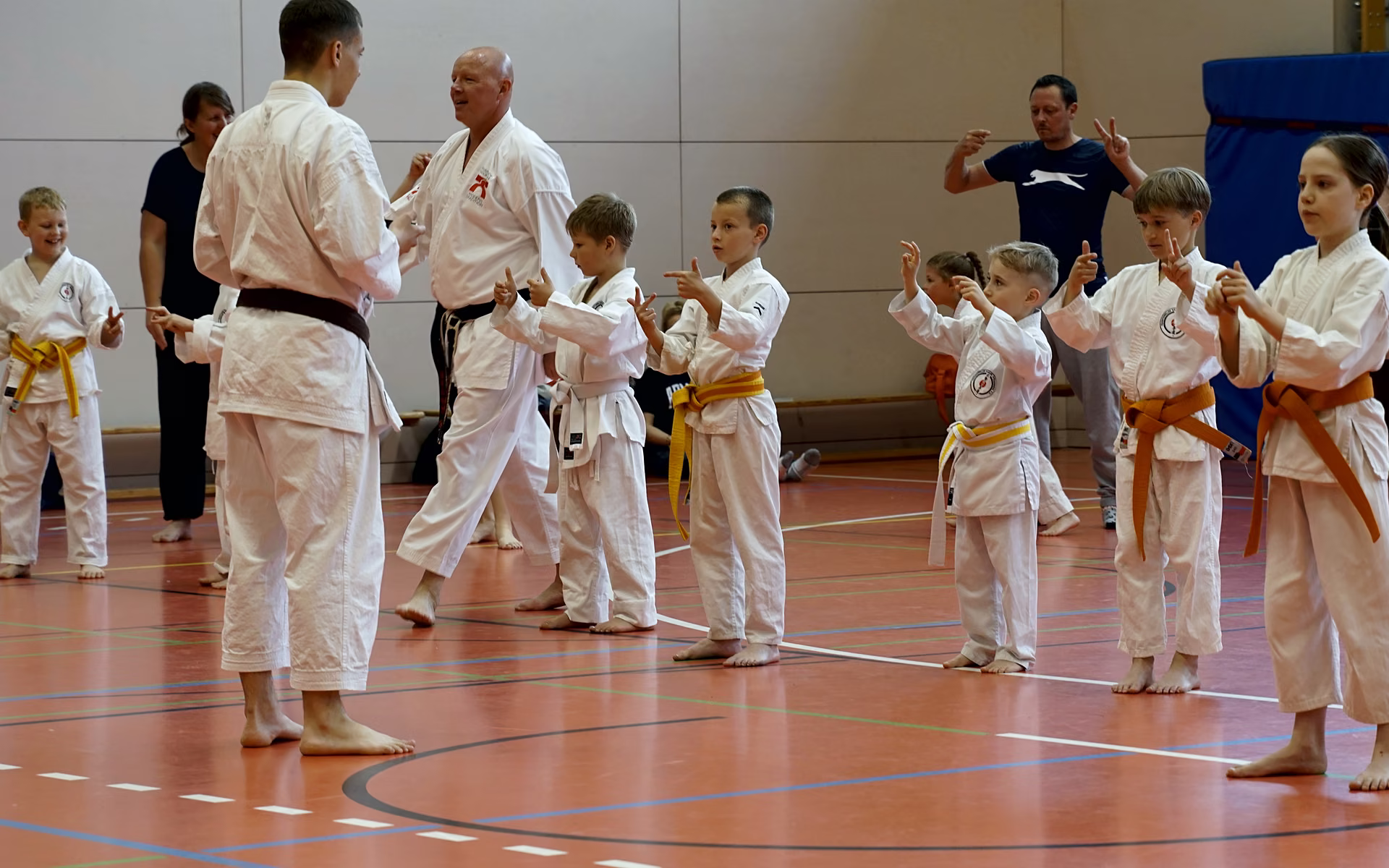 Kinder mit Gelb- und Orangegurt &uuml;ben in der Halle gemeinsam mit ihren Trainern