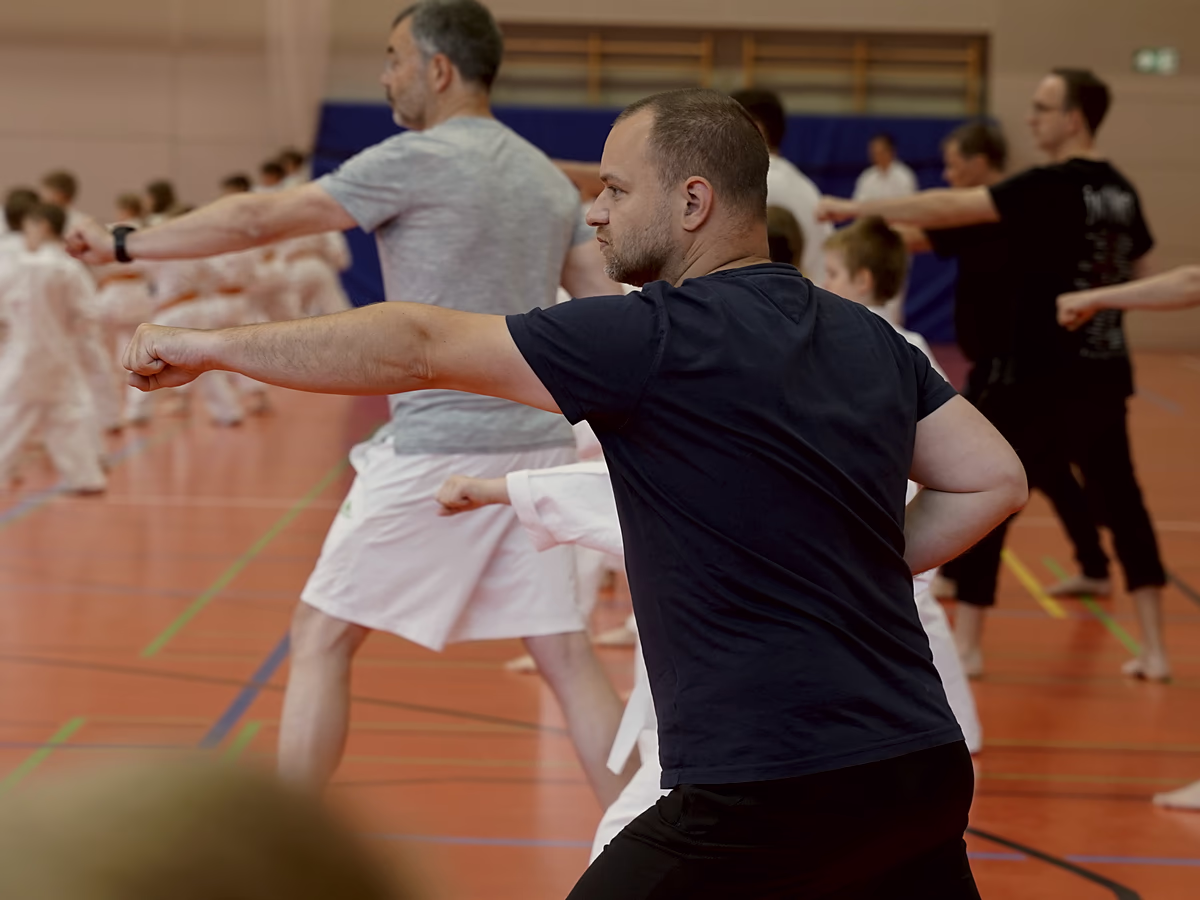 Zwei M&auml;nner in T-Shirt trainieren in der Reihe zwischen Karateka im Gi mit